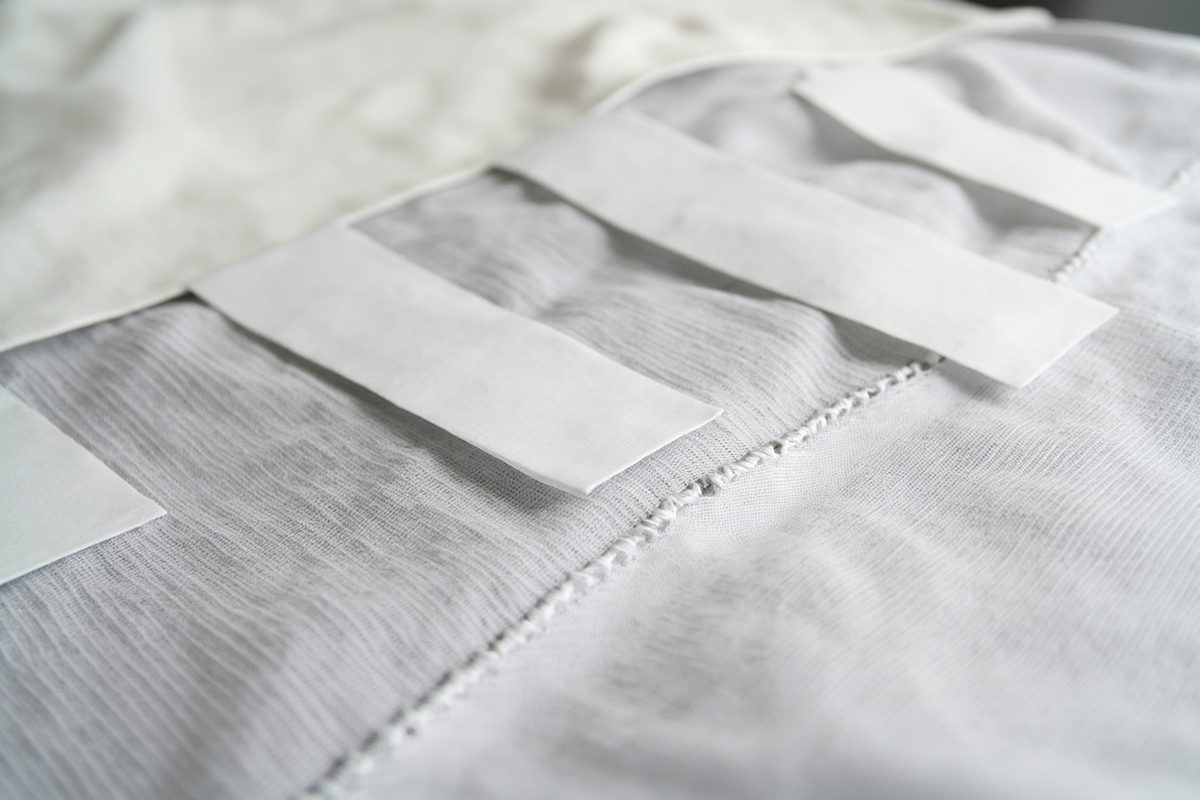 Pale fabric layers applied over a lighter panel, the raised edges catching the light and casting a shadow.