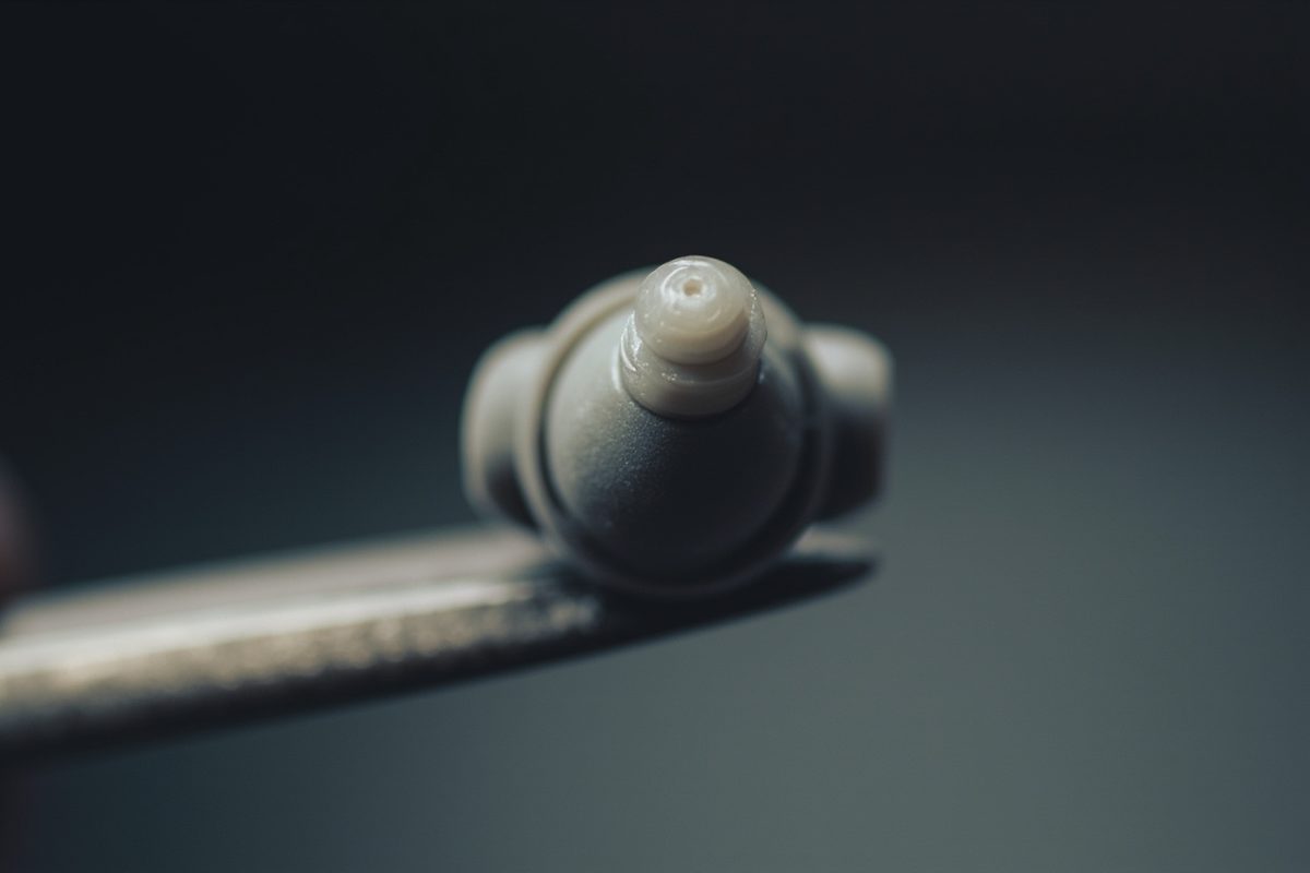 Extreme close-up of an unpainted plastic ball-and-socket joint held in tweezers, showing the moulding seam.