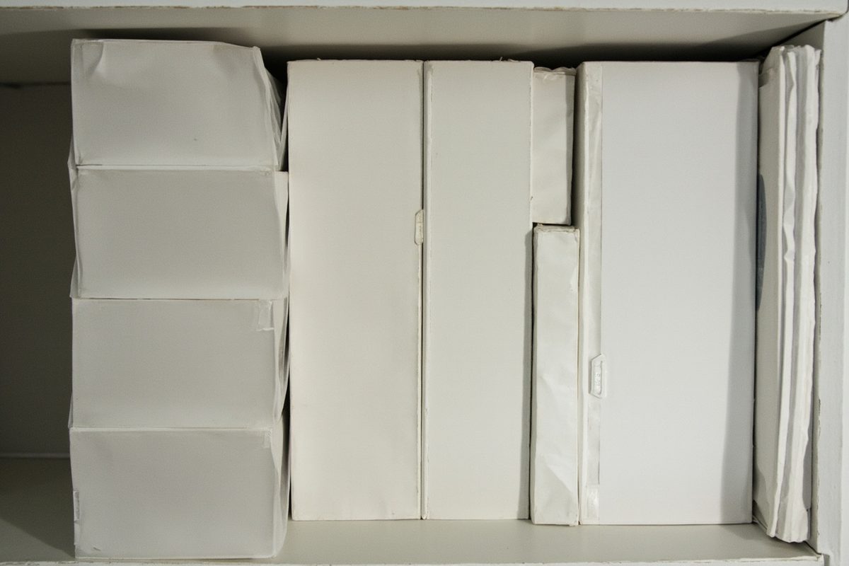 Blank rigid archival sleeves and acid-free storage boxes stacked upright on a dim shelf.