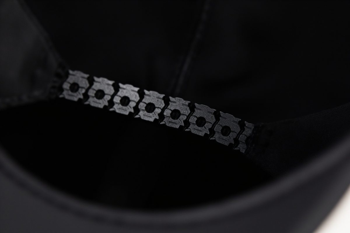 Close-up of the back of a plain baseball cap, showing an adjustable plastic strap fastened through a row of moulded peg holes.
