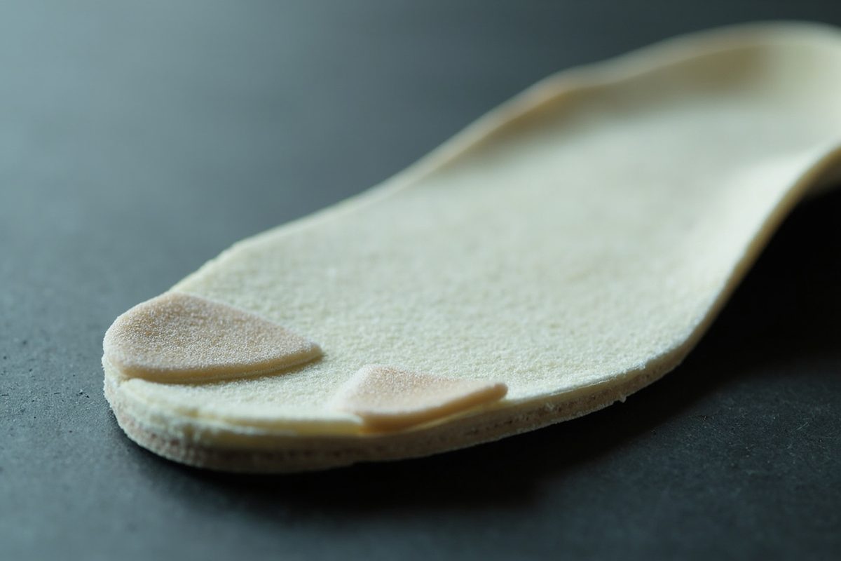 A plain unbranded foam shoe insole on a dark surface, its forefoot area darker and more compacted than the rest.