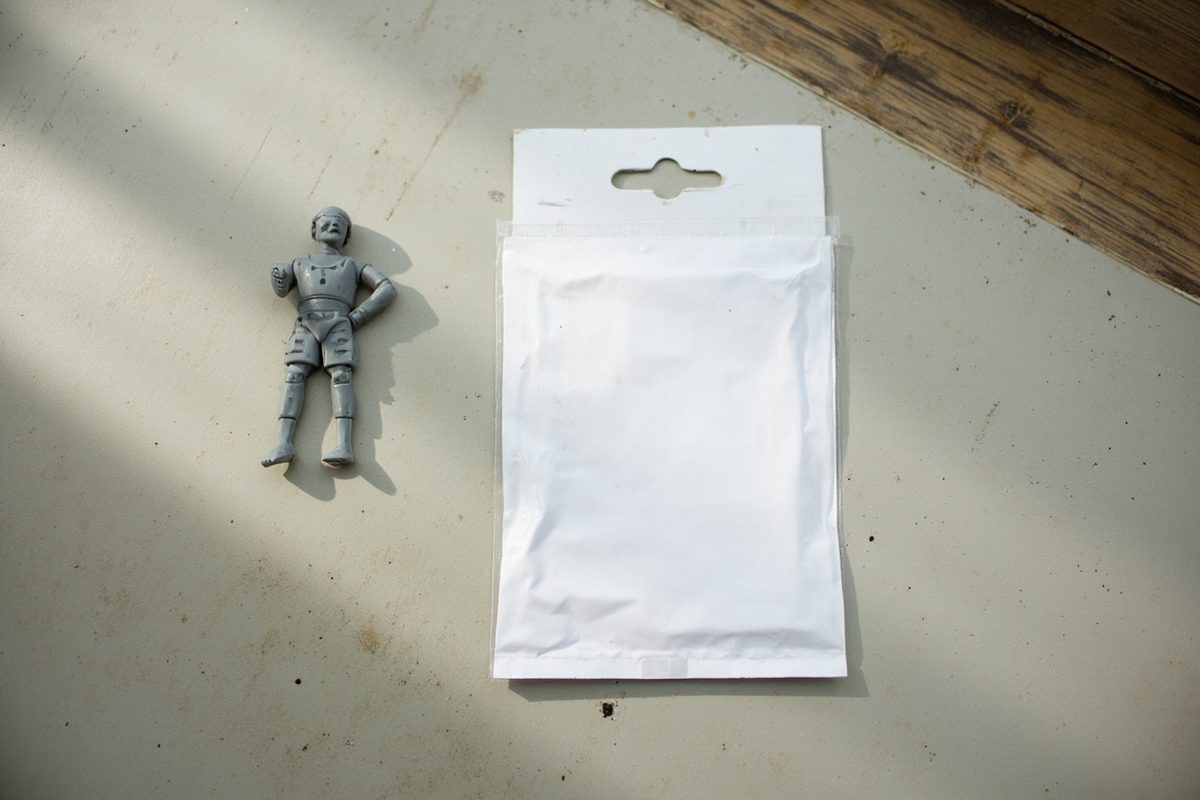 A loose grey plastic figure lying beside a blank unprinted packet with a hanging hole, photographed from above.