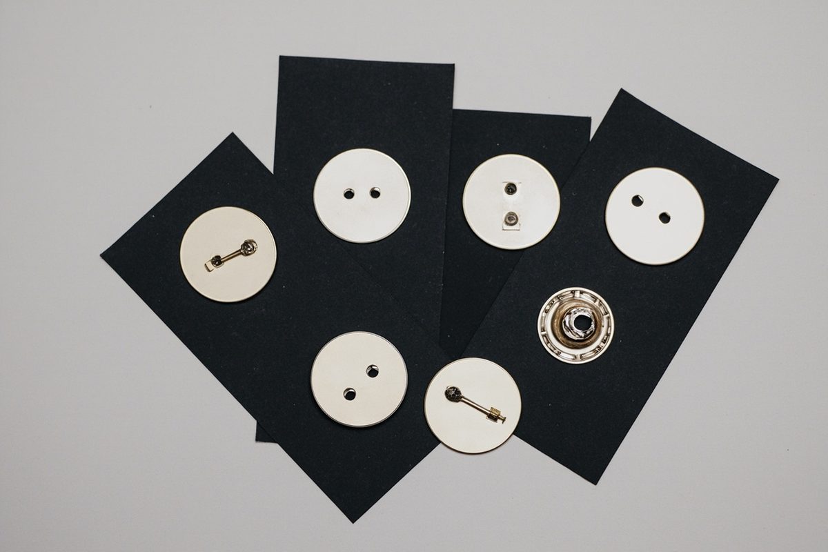 Several blank metal pin blanks laid face down on dark card, showing posts, clutches and flat unstamped backs.