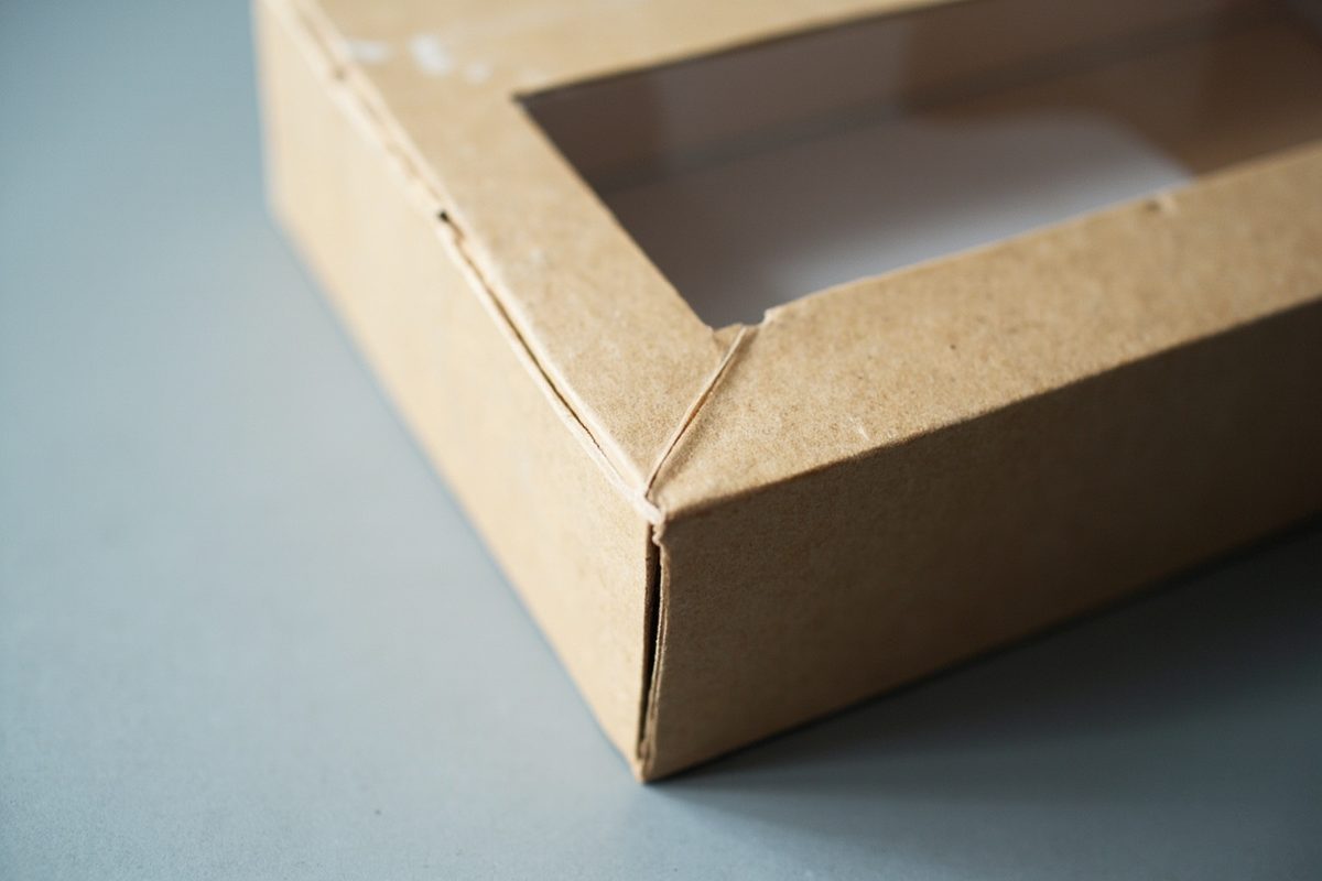 A plain unprinted window box at a three-quarter angle under raking light, showing corner wear and a dent.