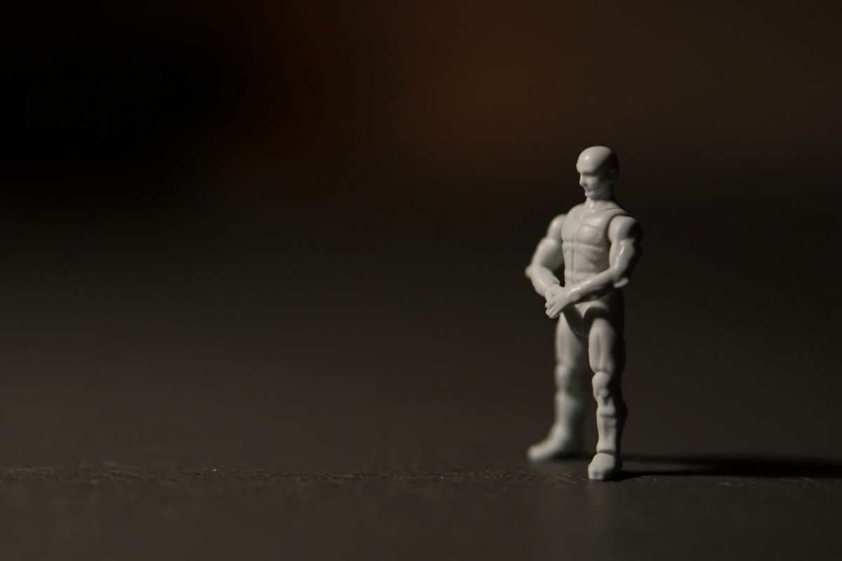 A plain unpainted grey articulated action figure standing on a dark surface with its joints and seams visible.