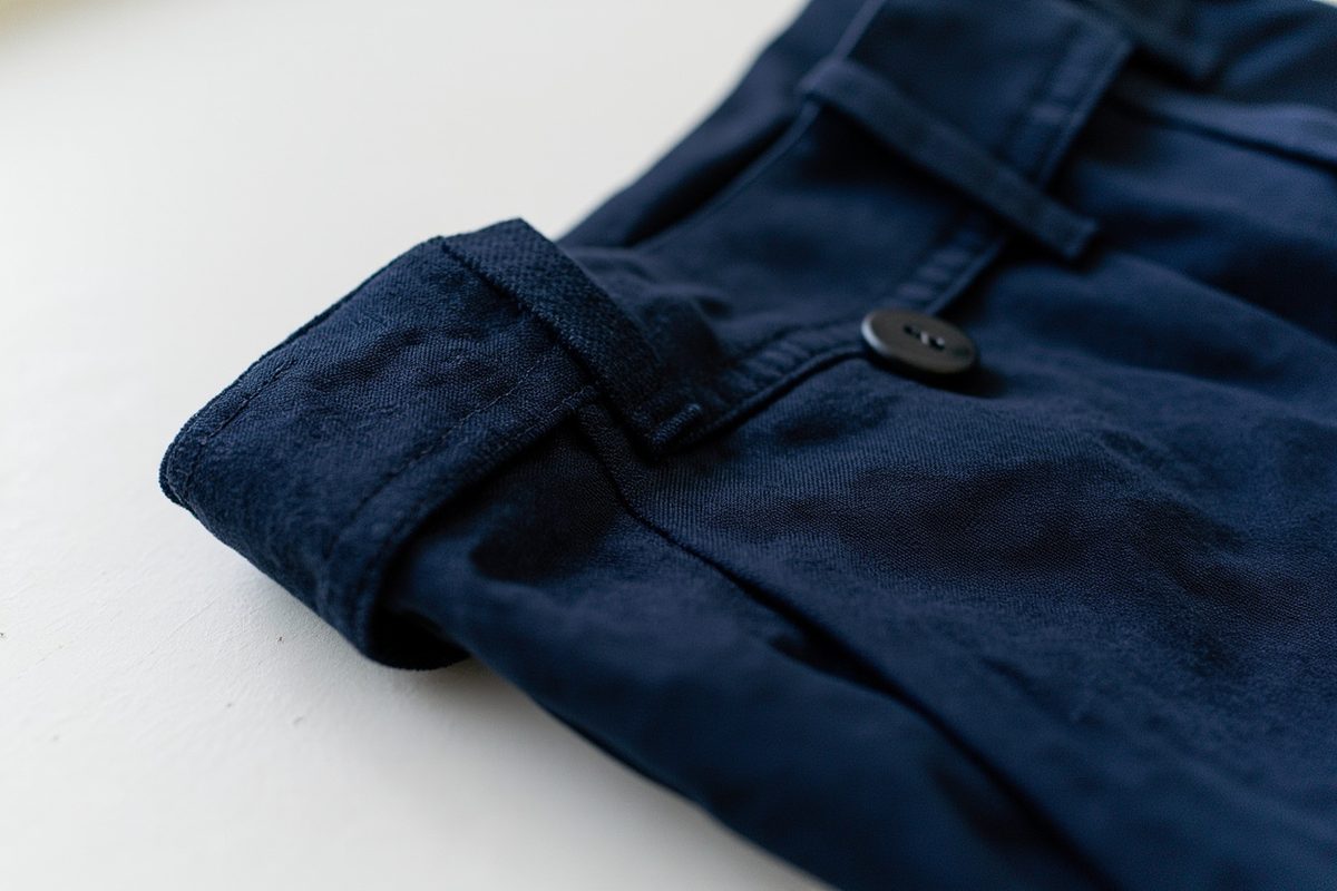 Close-up of the waistband corner, belt loop and topstitching of a pair of plain dark navy trousers.