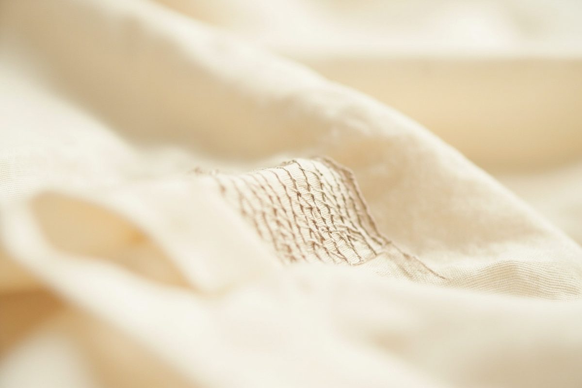 Close-up of a neat hand-darned square repair in plain pale fabric, the darning thread slightly different in tone from the cloth.