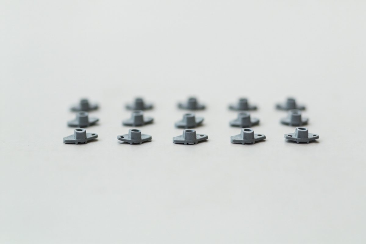 Neat rows of identical small unpainted grey plastic parts laid out and photographed from above.