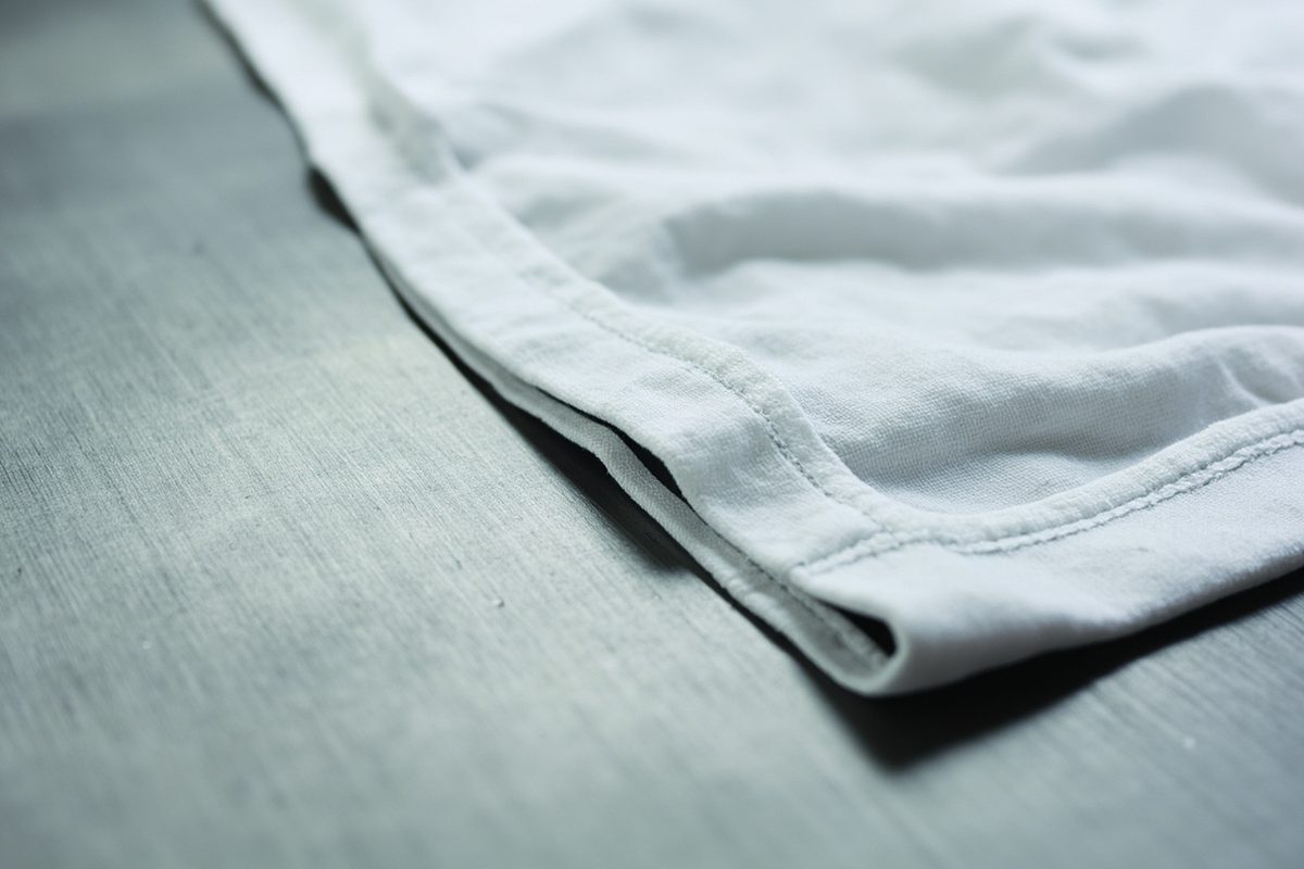 Close-up of the folded-back bottom hem of a plain white t-shirt, showing the stitched hem edge.