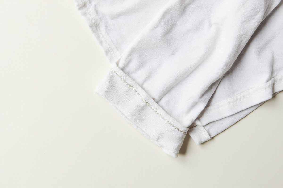 Close-up of a plain white t-shirt sleeve hem, with a single row of stitching running along the folded edge.