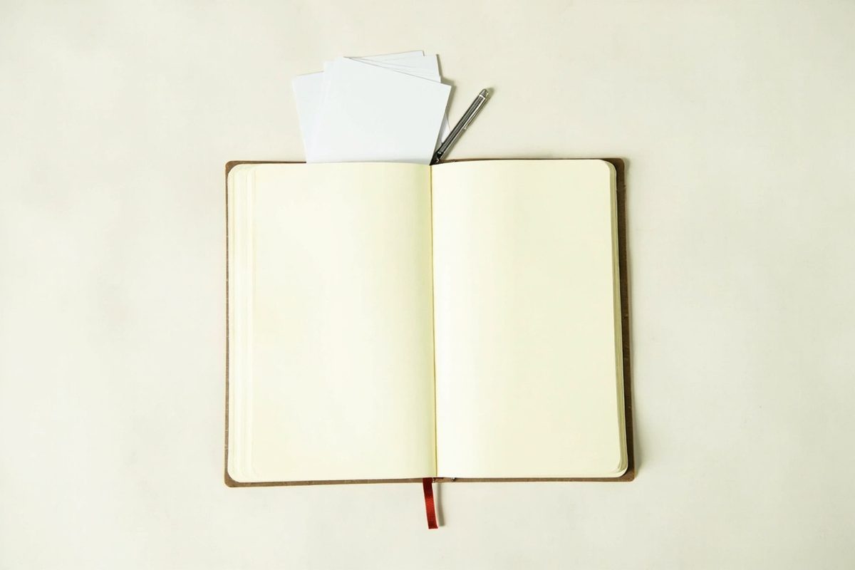An open notebook with blank pages, a pen and a few plain unmarked white cards on a pale surface.