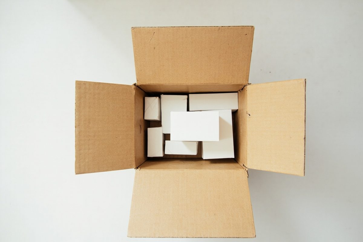 A cardboard box on a floor filled with plain unmarked objects of the same rough size, seen from above.