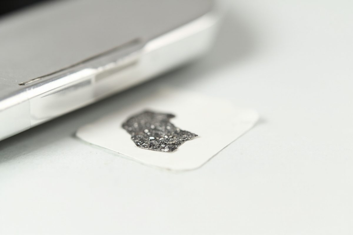 A blank white sticker with a patch of flaked reflective foil lying beside the edge of a chromed plastic part on a white surface.