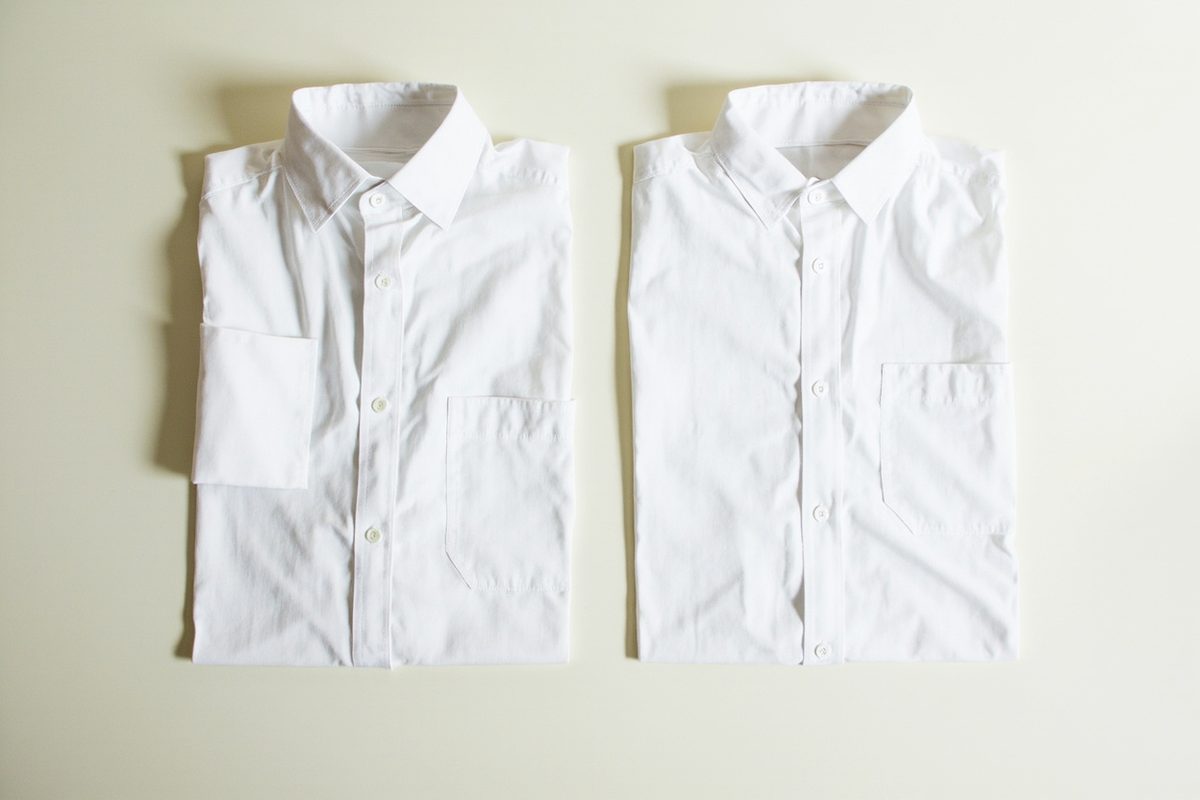 Two plain white shirts folded and laid side by side on a pale surface for comparison.