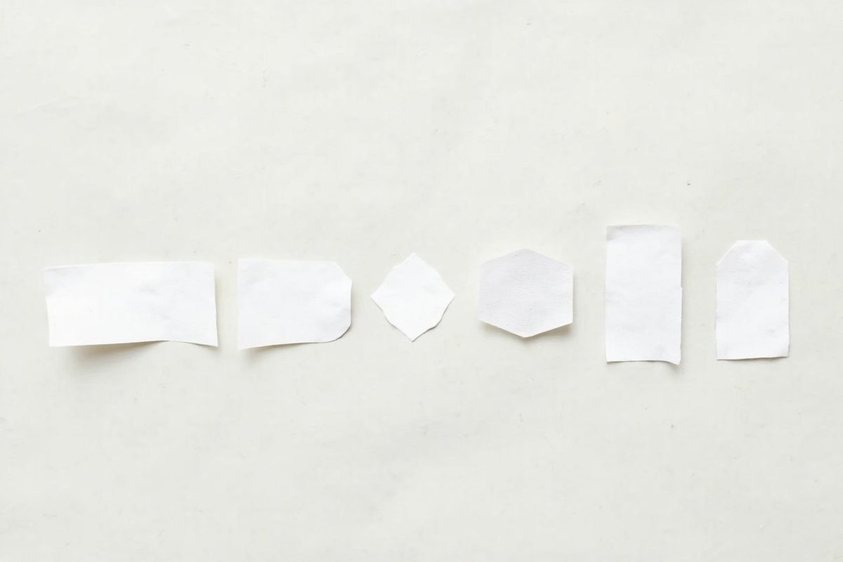 Several blank garment size labels of different shapes laid out in a row on a pale surface.