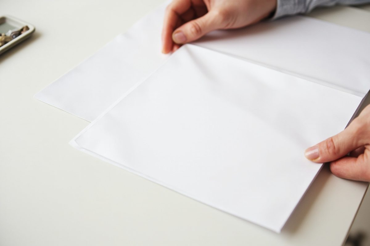 A plain paper booklet being slid into a clear sleeve with a white backing board on a desk.