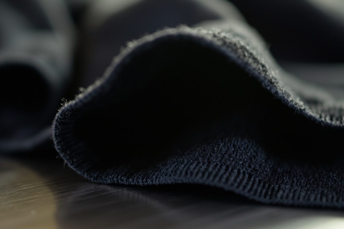 Extreme close-up of soft dark cotton jersey folded to show the knit edge and the hand of the cloth.
