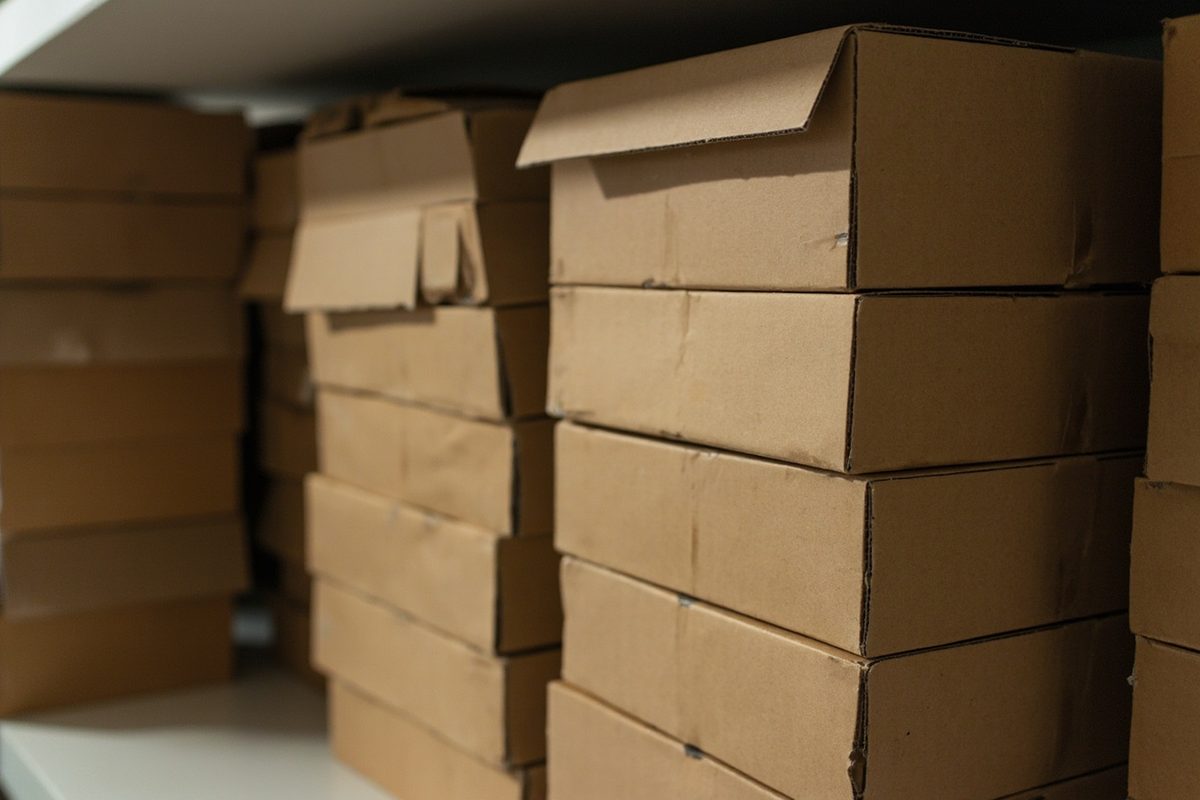 A dense shelf of identical plain unprinted cardboard boxes stacked several deep in a dim storeroom.